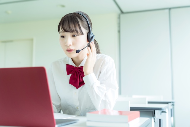 教室でオンライン英会話のレッスンを受ける髪を括った女子高校生