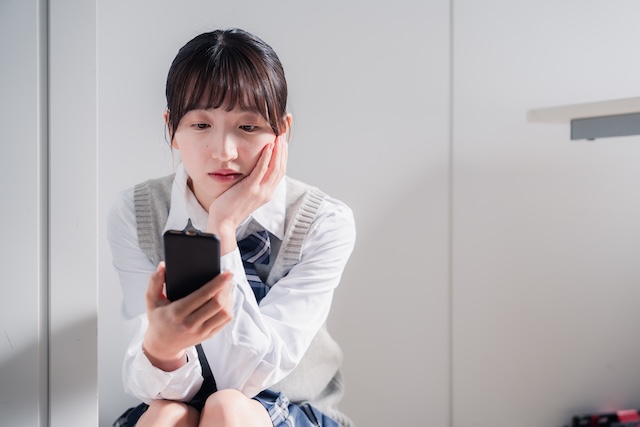 スマートフォンを見つめて落ち込む女子高校生