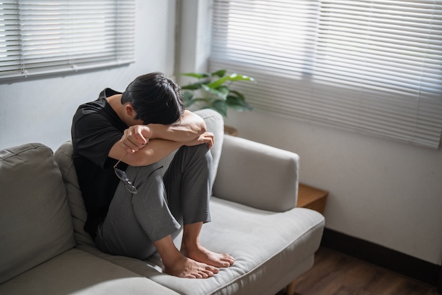 ソファーの上で悲しそうにうずくまる男性