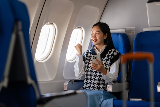 機内でスマートフォンを見てガッツポーズをする女性