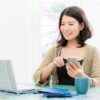 ノートパソコンを見ながらスマートフォンで申し込む女性